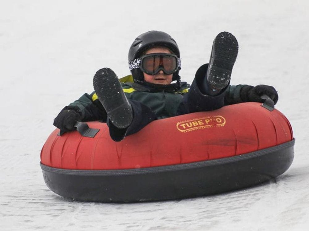 A young child wearing snowgear, including a black helmet and goggles, sits on a red snow tube at Copper Mountain, one of the best Colorado snow tubing spots!