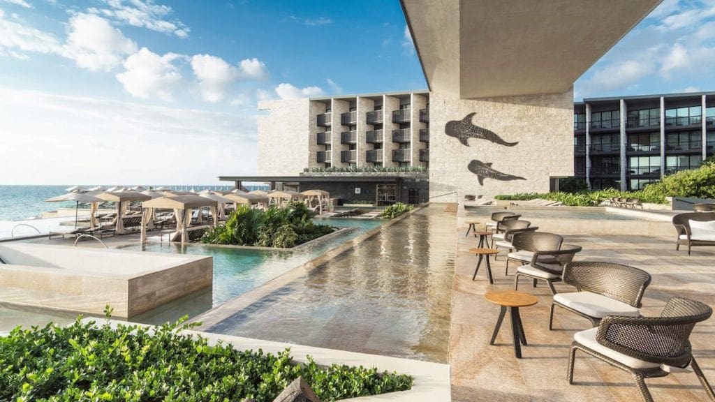 Inside the Grand Hyatt Playa del Carmen, featuring several seated areas, a pool, and a glimpse at the ocean access.