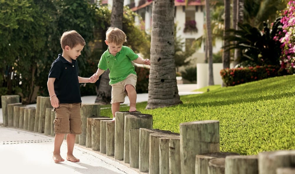 An older boy helps his young brother walk along a short fence at Grand Velas Riviera Maya.