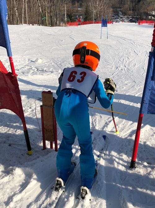 A young skier wearing a blue suit and orange helmet sports the number 63 in a ski race at Catamount Ski Resort.