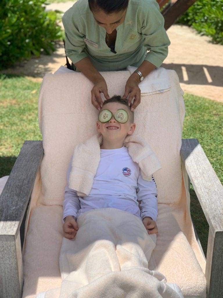A young boy with cucumbers on his eyes enjoys a kid-friendly massage on-site at Rosewood Mayakoba.