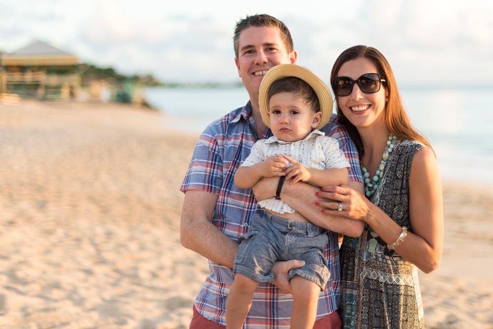 A family of three smiles on the beach in Antigua, one of the best Caribbean islands for families.