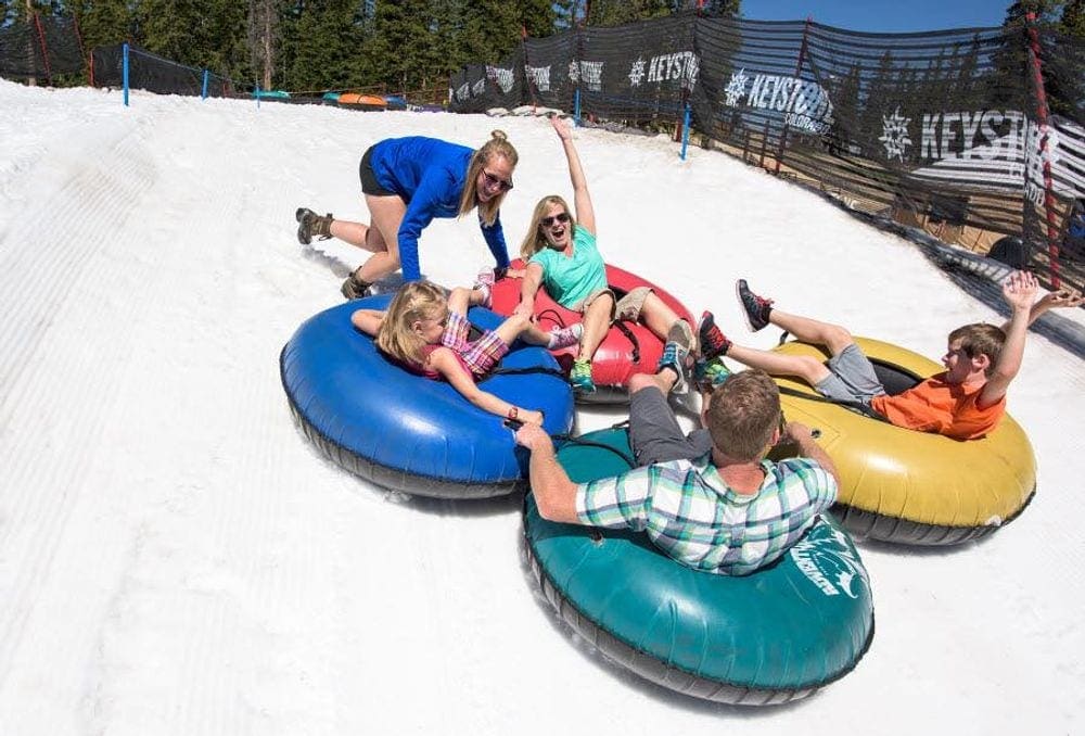 Four snow tubes are connected as a family of four is pushed by a staff member down a snowy hill at the Keystone Resort, one of the best Colorado snow tubing spots!
