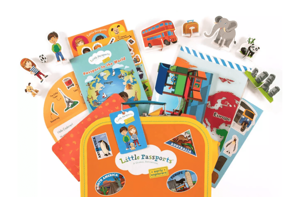 A Little Passports product shot, including an orange suitcase with books, toys, and other items spilling out.