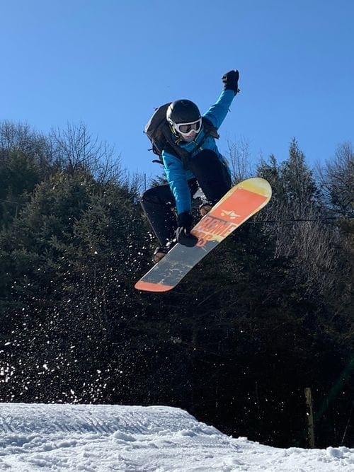 A young boy takes a huge jump on a snowboard.