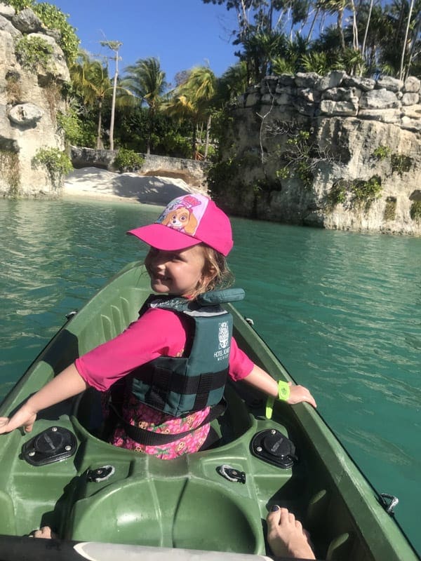 A young girl sitting in a canoe looks back smiling at the camera while they glide through the water near Hotel Xcaret Mexico.