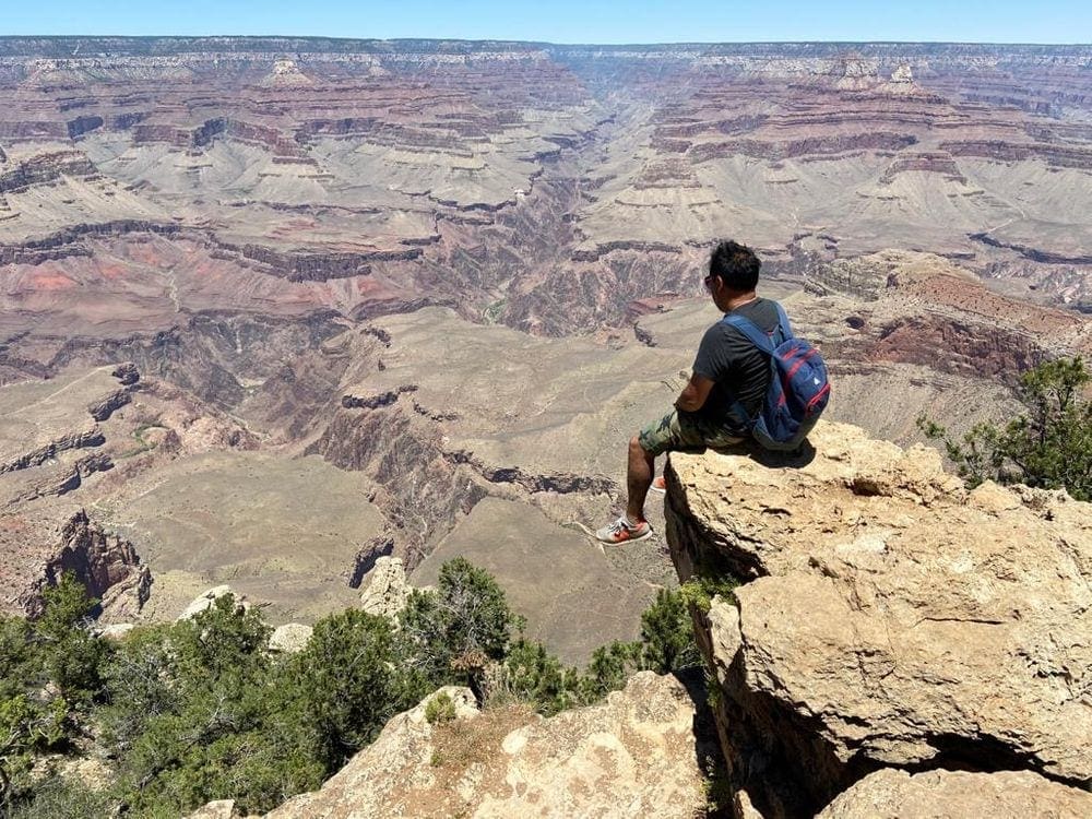 A man sits along a cliff in the Grand Canyon.