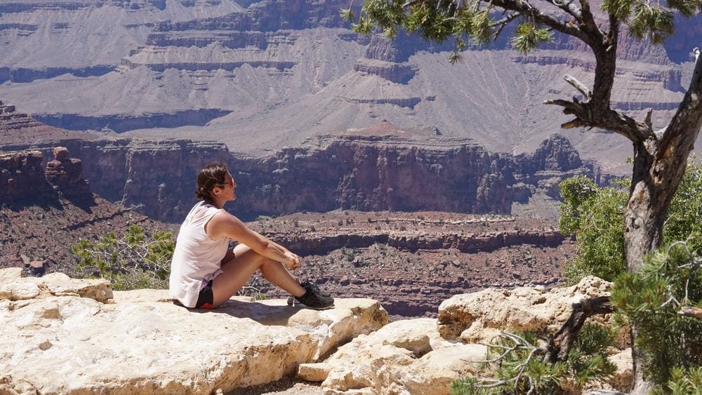 A woman sits with a sweeping view of the Grand Canyon behind her.