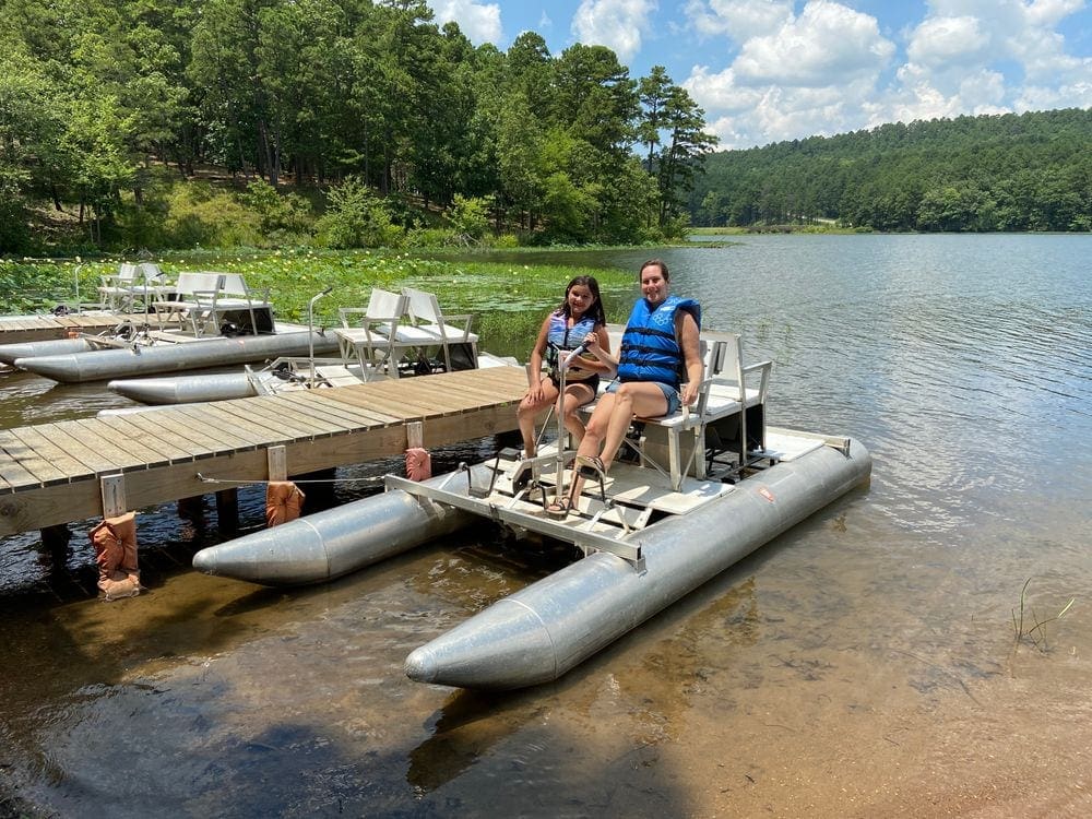 A mom and daughter sit on a paddle boat in the Ozarks wearing proper swimware and life-jackets, essential on our list of packing tips for COVID travel.
