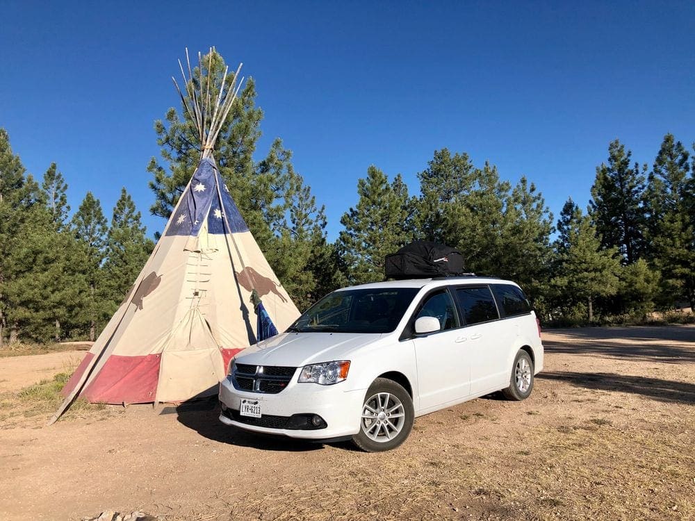 A white van is parked in front of a tipi.