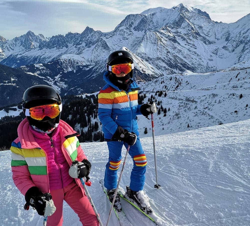 Two kids in full colorful ski gear, including ski goggles and helmets, knowing where to buy ski gear can help plan a family ski trip on a budget.