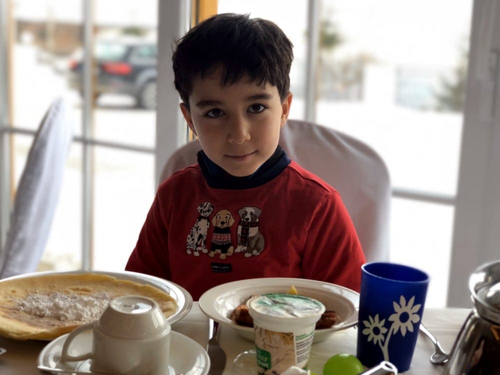 A young child sits in a restaurant with a table full of goodies. Knowing how to prepare for eating out is one of our tips for traveling with children who have allergies.