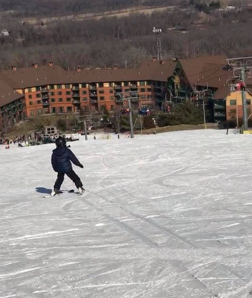 A young boy, wearing all black, skis down the bunny hill toward the lodge at Mountain Creek, one of the best ski resorts near NYC for families.