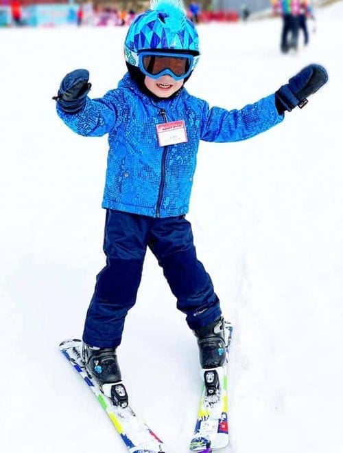 A young boy wearing all blue gleefully skis at Mount Peter.