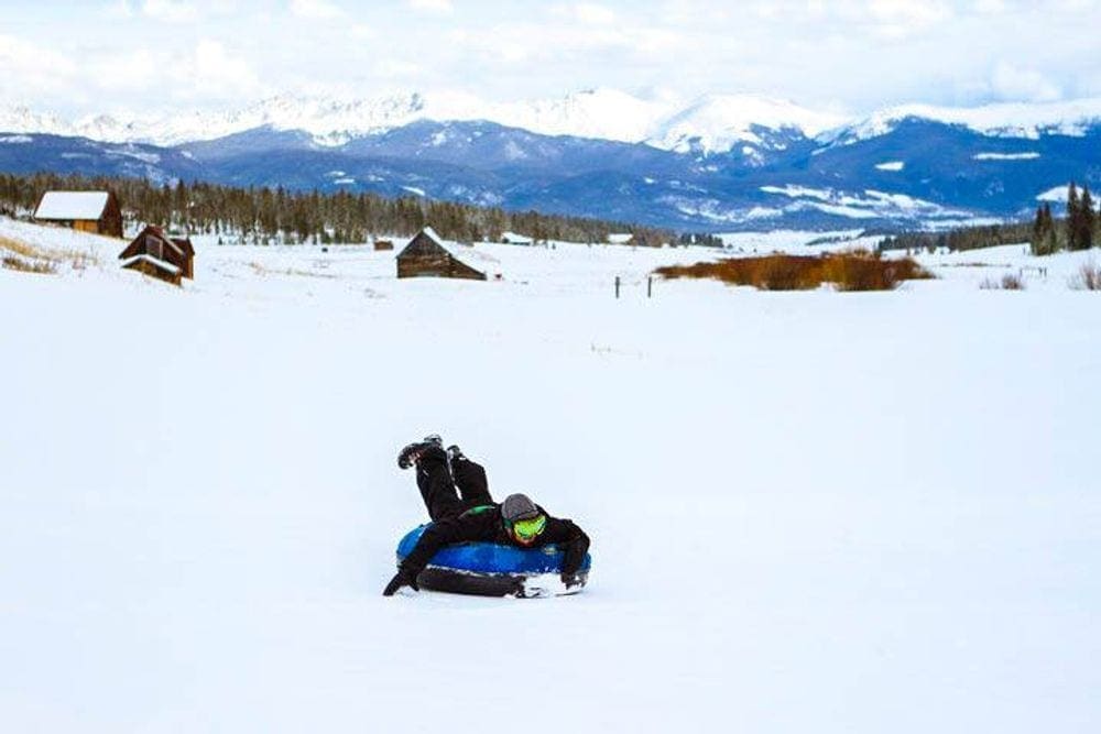 A teenager rides on a snow tube on his stomach down a hill at the YMCA of the Rockies, one of the best Colorado snow tubing spots!