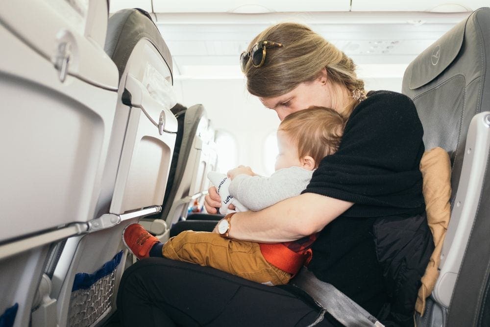A mom holds her infant son on an airplane, knowing your airline options is just one of the things on our list of travel resources for families.