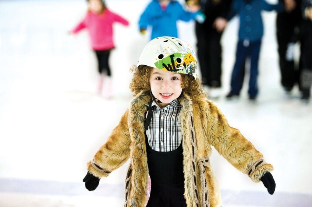 A young girl wearing a brown coat and helmet skates at Chelsea Piers Sky Rink.