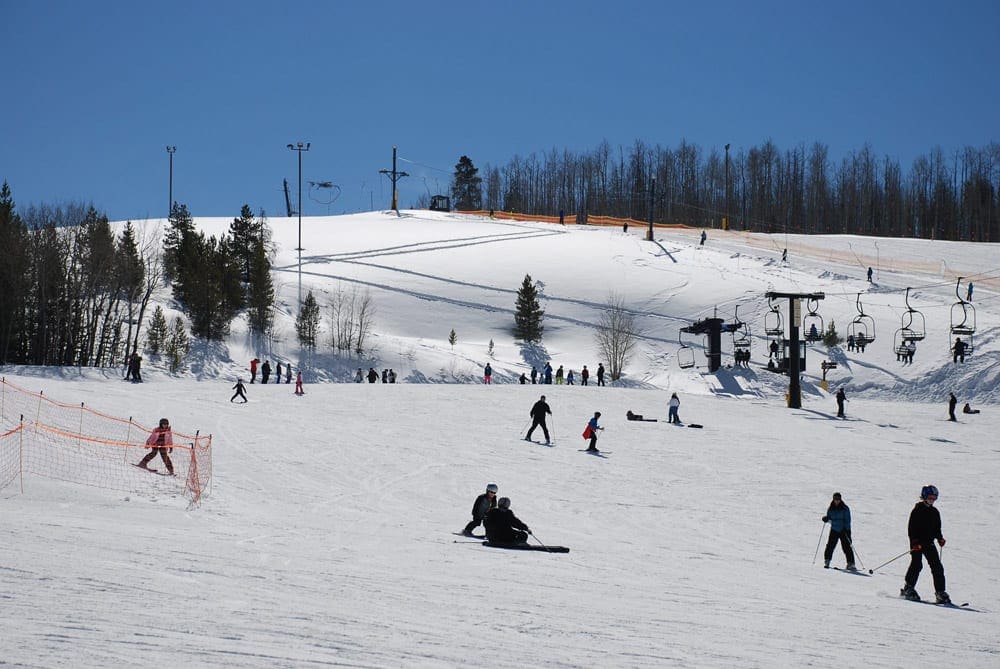 A view of the slopes at Granby Ranch, featuring dozens of skiers and a chair lift.