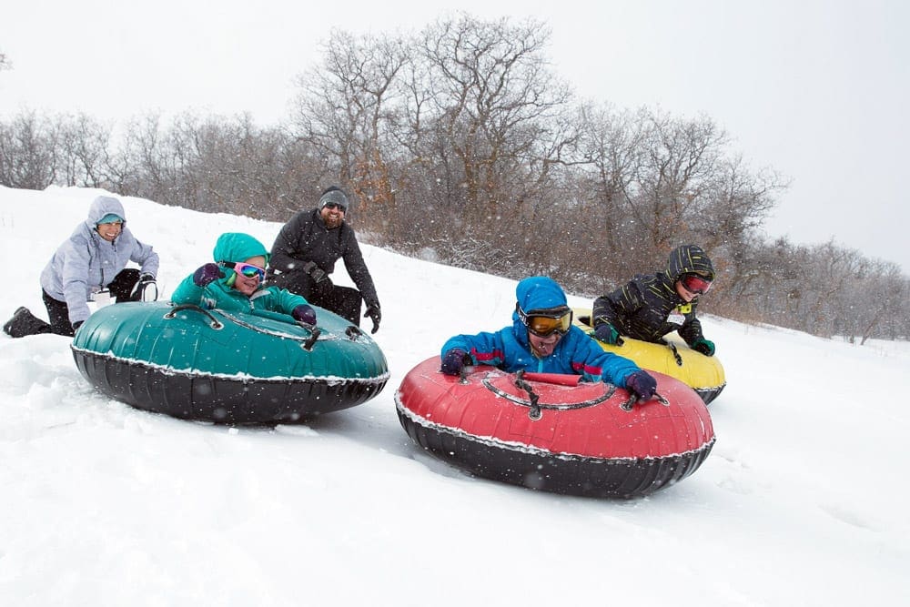 Three colorful tubs hold individual riders, while two additional people run behind them at Hesperus, best small ski resorts in Colorado for families.