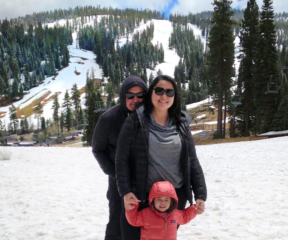 A family of three stands in the snow in Lake Tahoe.