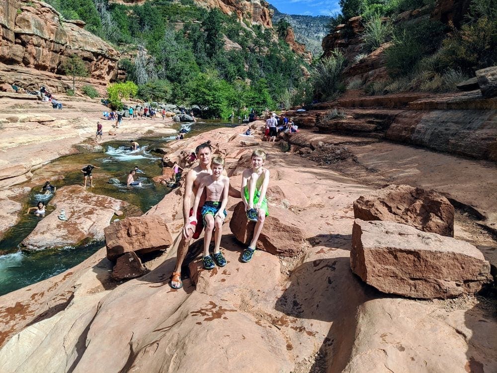 A dad and two boys sit in the sun by Slide Rock State Park in Sedona, Arizona, a must see on any Sedona itinerary for families.
