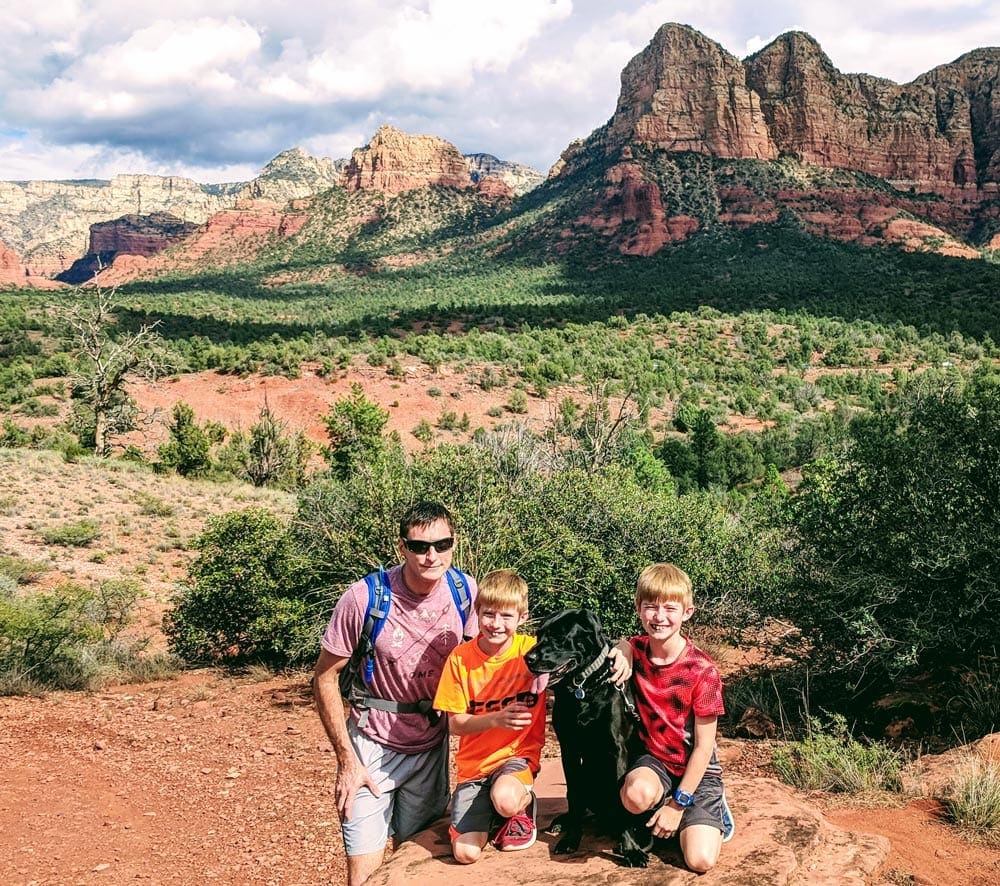 A father and his two sons sit on a large rock in the Sedona desert.