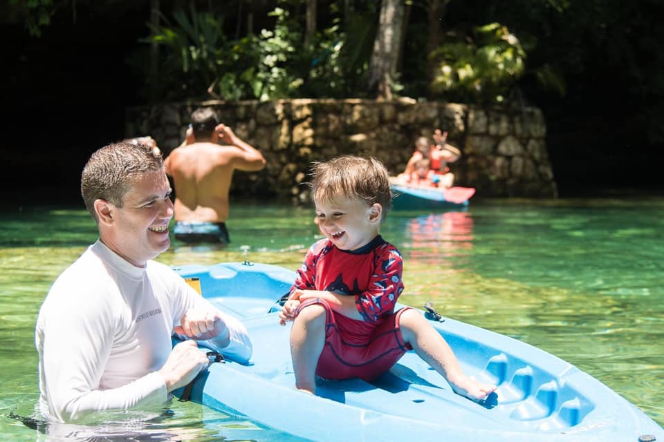 A dad holds onto a paddleboard holding his young son in a cenote in Playa del Carmen.