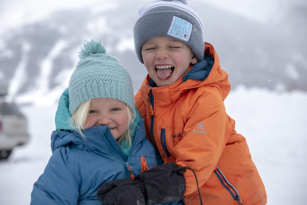 A young boy hugs his little sister, both are wearing colorful snow gear in blue and orange, at Kendall Mountain.