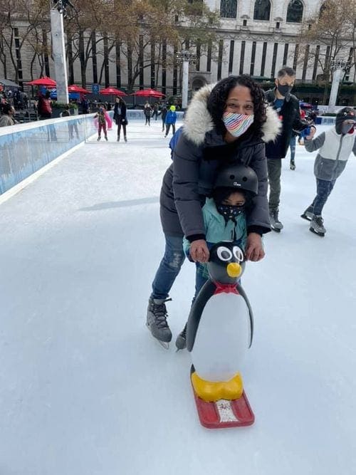 A mom holds onto her young child as they use an iconic penguin at Bryant Park to go ice skating.