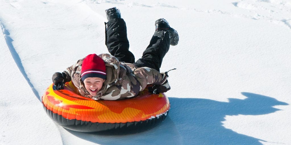 A young boy slides down a slope at Nemacolin Woodlands Resort on an orange snow tube.