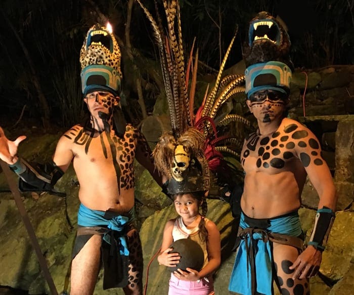 A young girl stands with two performers at Xcaret Eco Park.