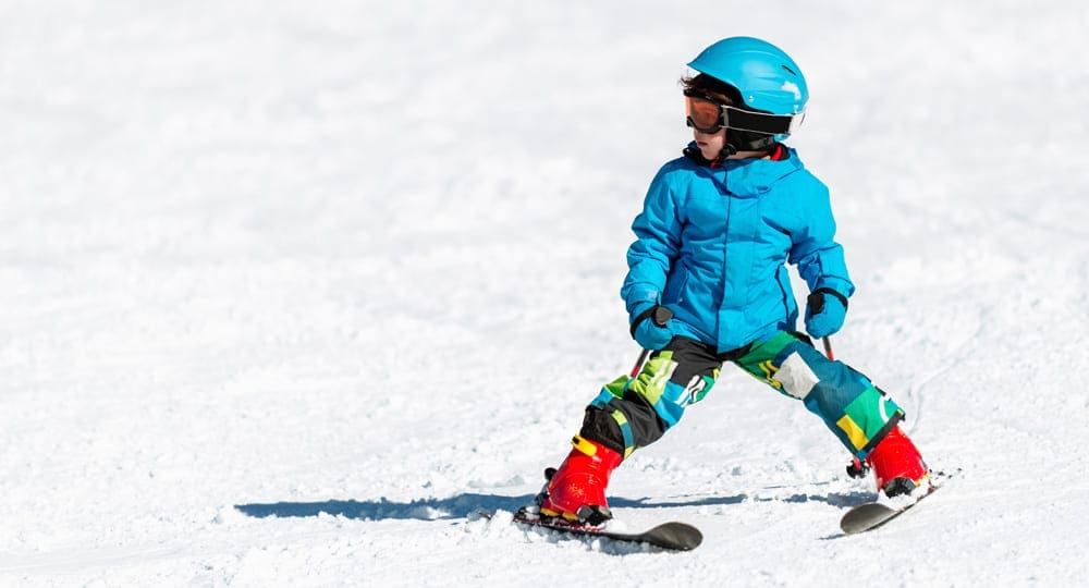 Child wearing blue jacket and helmet learning to ski on the slope.