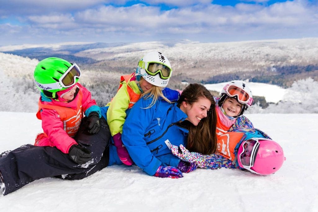 A ski instructor plays in the snow with four happy little girls outfitted in full snow gear at Snowshoe Mountain Resort, one of the best options for skiing near DC with kids.
