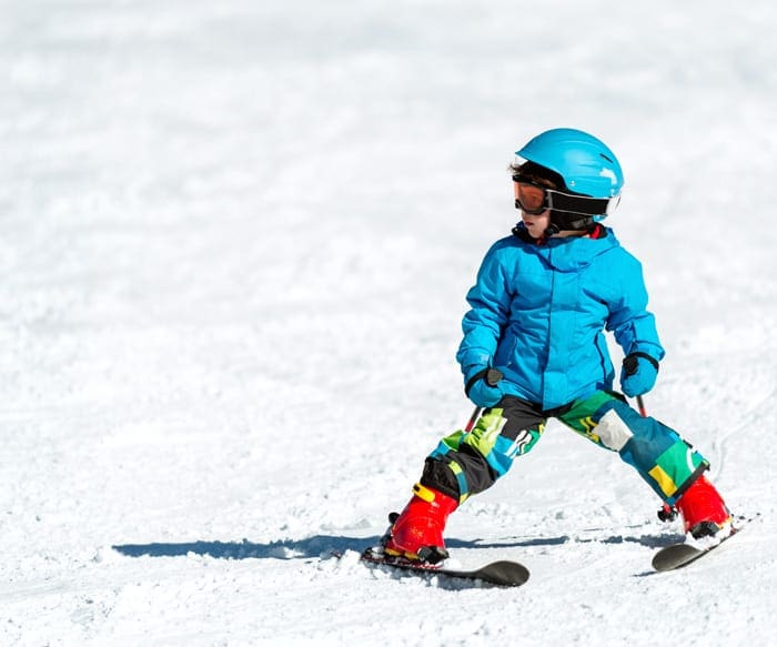 kid wearing blue jacket and helmet learning to ski on the slope