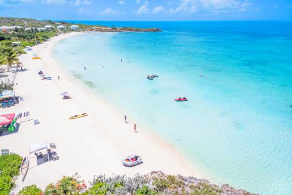 Aerial view of Sapodilla Bay, featuring turquoise waters, white sand beaches, and a number of beach-goers.