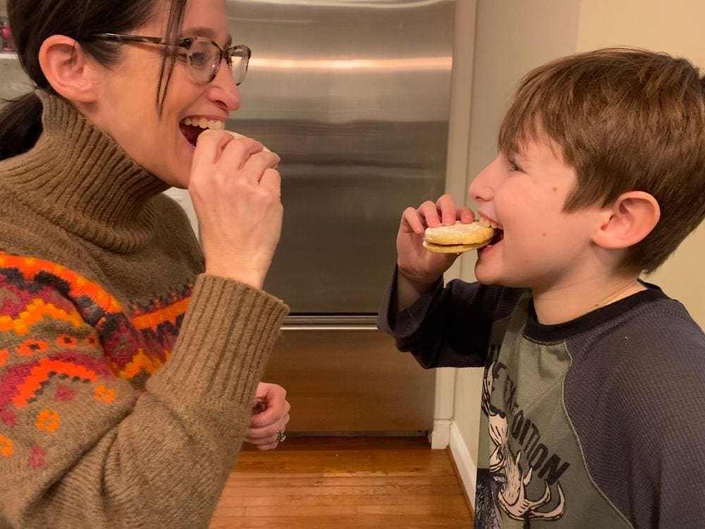 A mom and son both bite into Argintine cookies, one of the featured recipes from around the world, while looking at eachother.