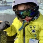 A young boy wearing a yellow jacket and ski goggles rides a chair lift at Shawnee Resort.