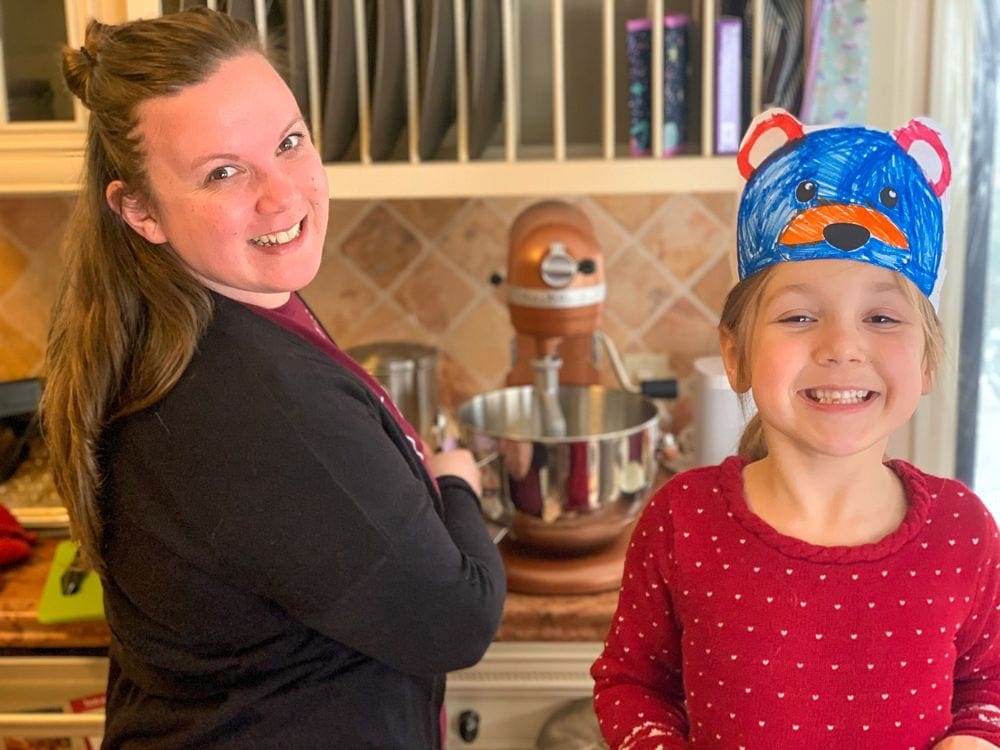 A mom and young girl turn around to smile while baking in the kitchen.