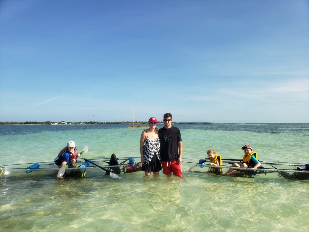 Two parents stand between two kayaks, both of which their chidlren are sitting in, near Key West.