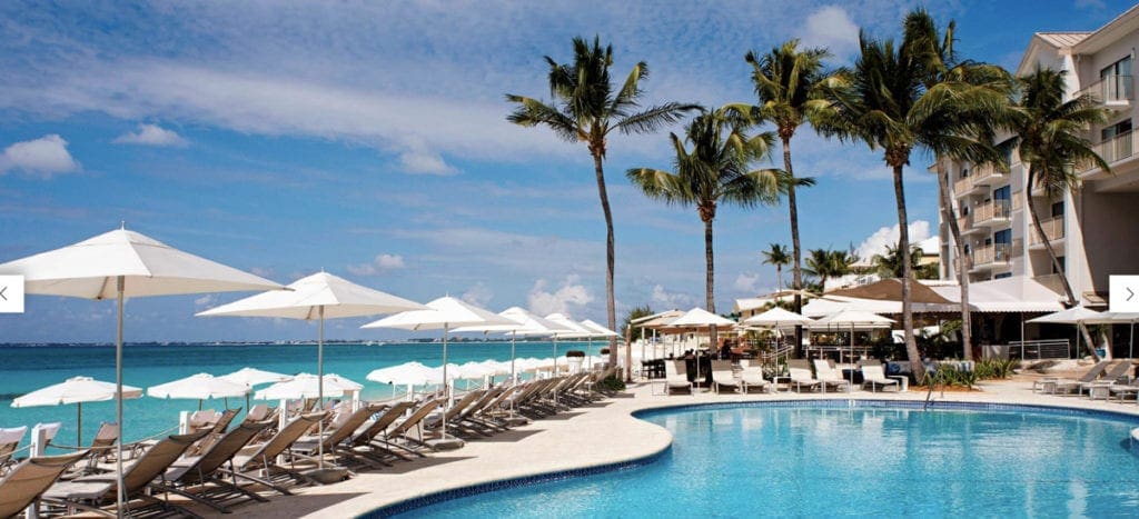 A pool at Grand Cayman Marriott Beach Resort, surrounded by beach chairs and palm trees.