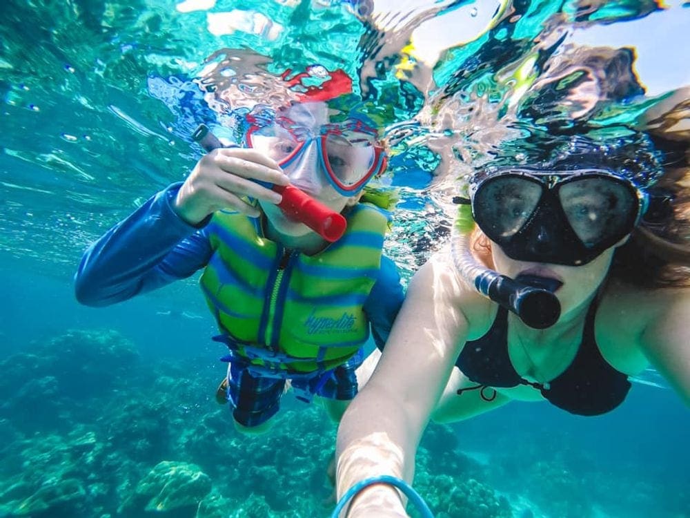 A mom and her young son snorkel near Ko Tao in Thailand. Practicing wearing the gear is one of our tips for snorkeling with kids.