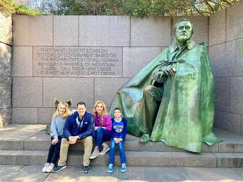 A family of four sits together near a statue in Washington DC, one of the best US cities for a Memorial Day Weekend with kids.