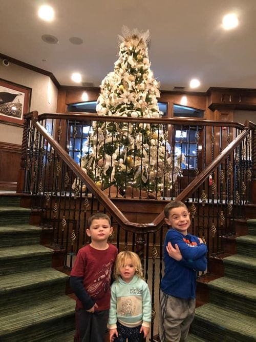 Three kids stand in front of the Christmas tree at Crystal Springs.