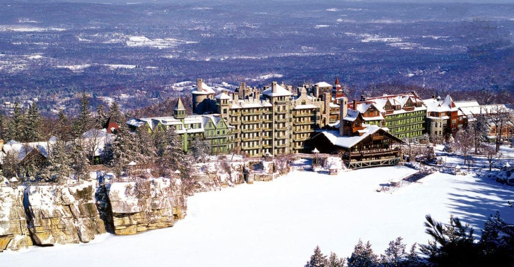 Aerial view of Mohonk Mountain House, one of the best family resorts near NYC for a winter getaway, during the winter, featuring clear blue skys and snow.
