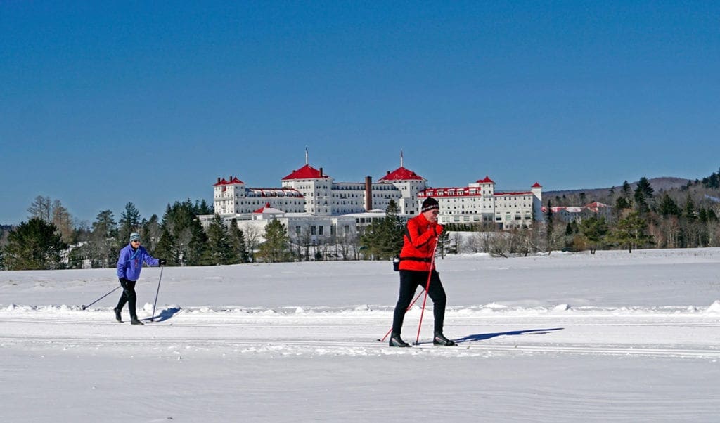 Two cross-country skiers traverse a frozen lake in front of the Omni Mt. Washington.