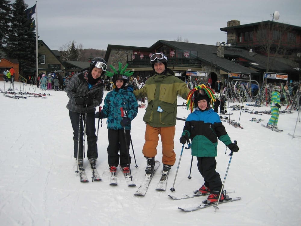 A family of four stands outside the chalet at Mount Snow Resort, one of the best family ski resorts in Vermont.