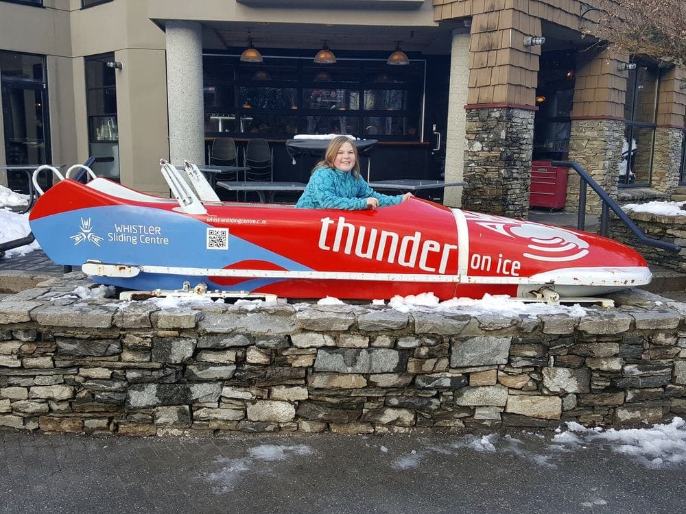 A young girl sits in a bob sled in the center of Whistler Villiage.
