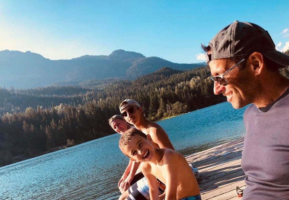 A family of four laughs as they sit on a dock on a lake near Whistler.