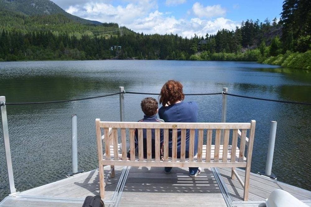 A mom and her young son sit on a bench admiring a lake in British Colombia.