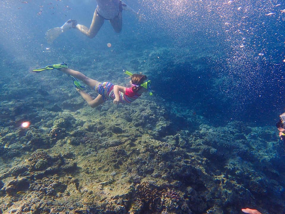 A young child snorkels underwater with proper flippers, an important component to kids snorkel gear, in Okinawa, Japan.